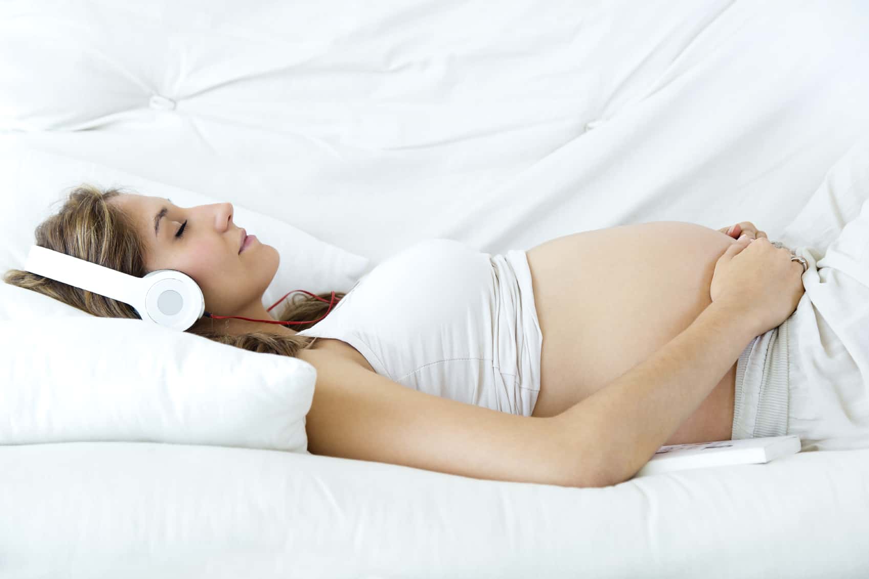 Massasjeterapi mot fødselssmerter 4 Portrett av gravid kvinne som sitter hjemme i sofaen og hører på musikk i hodetelefoner.