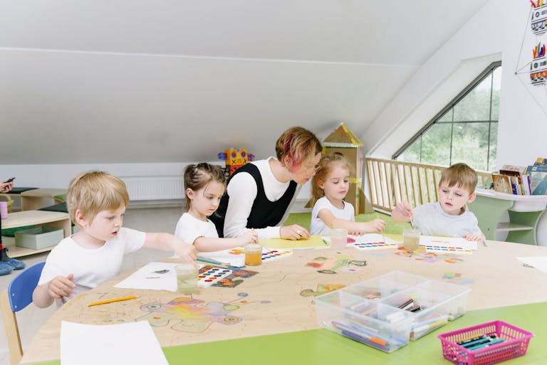 Young children engaging in art activities with a teacher in a bright kindergarten classroom.